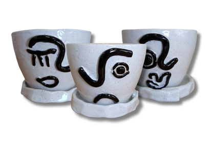 Rankų darbo keraminiai gėlių vazonai su juodais minimalistiniais veido piešiniais.