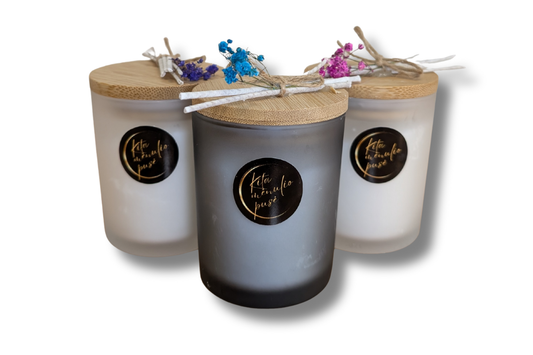 Rankų darbo smėlio vaško žvakė juodame stikliniame inde su mediniu dangteliu ir džiovintomis gėlėmis.